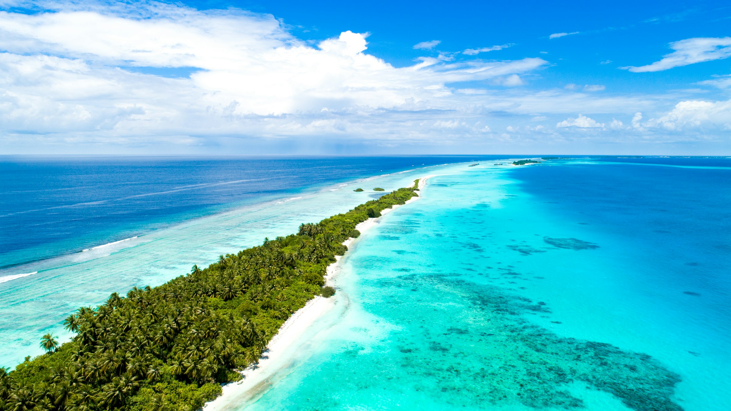 Aerial view of a palm-covered island strip between a turquoise lagoon and the deep blue ocean